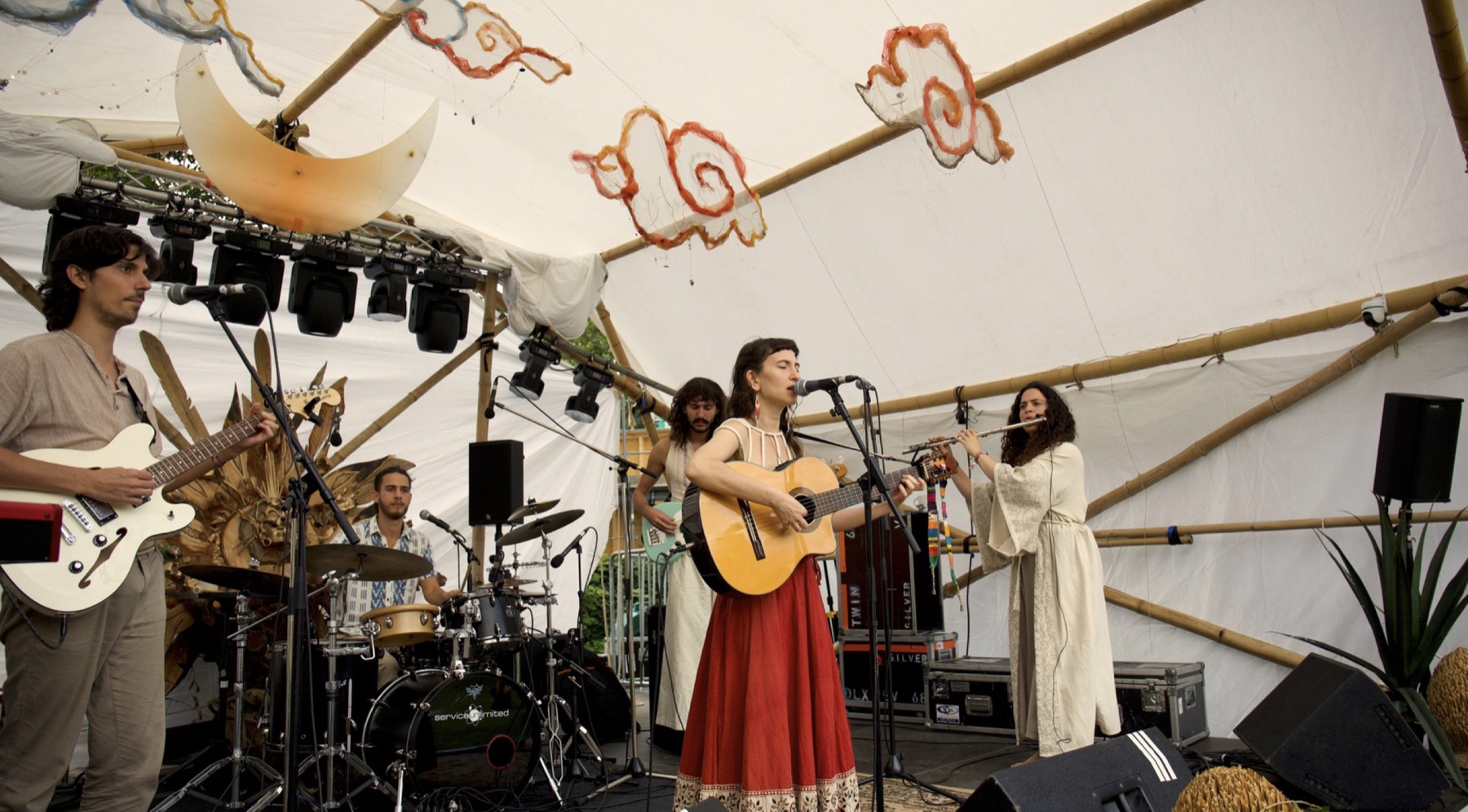 Cloud Of I playing on a festival stage under a white tent decorated with paper clouds and a crescent moon