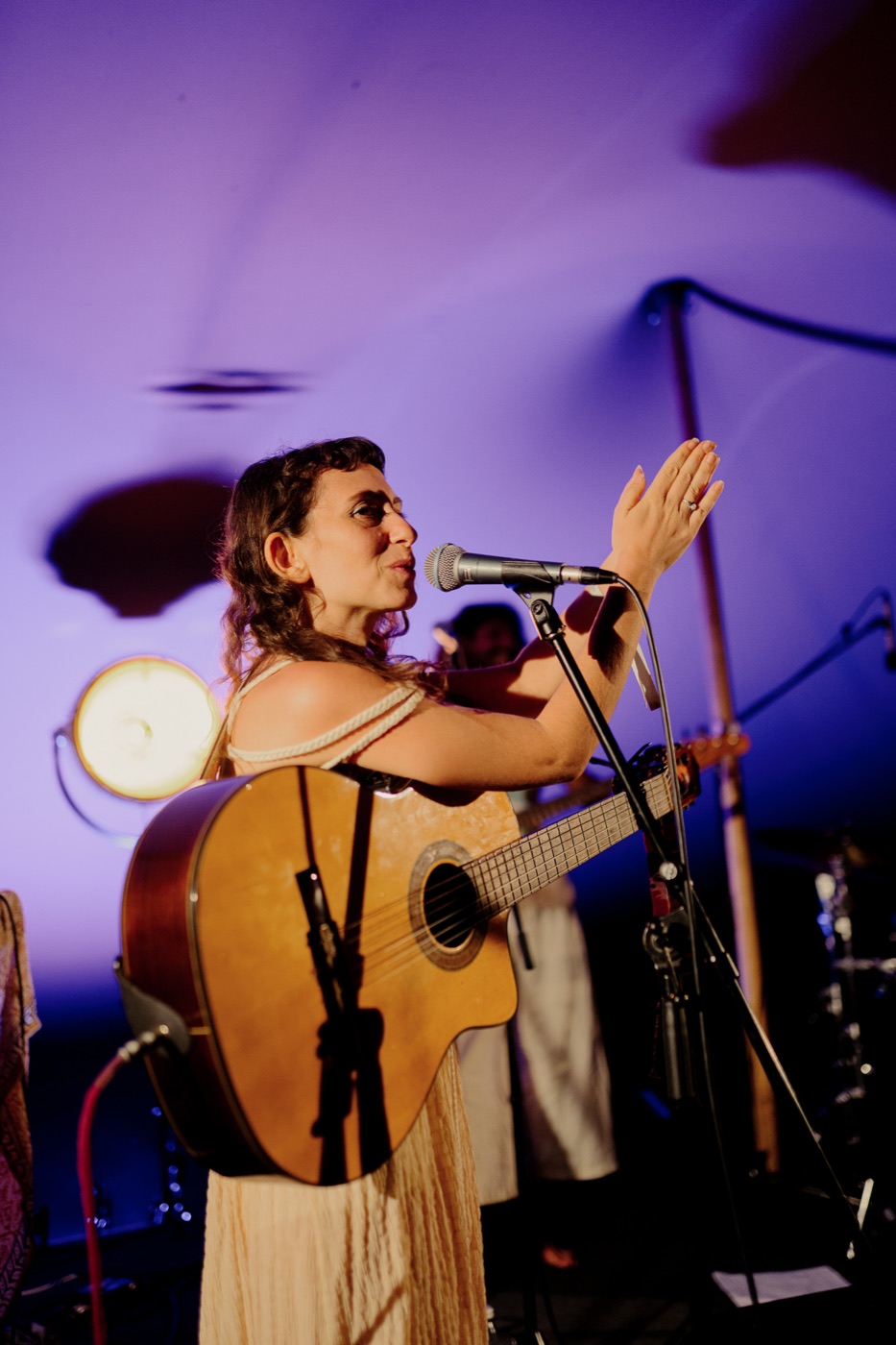 Yuli raising her hand while singing on the purple-lit stage at Guardians festival
