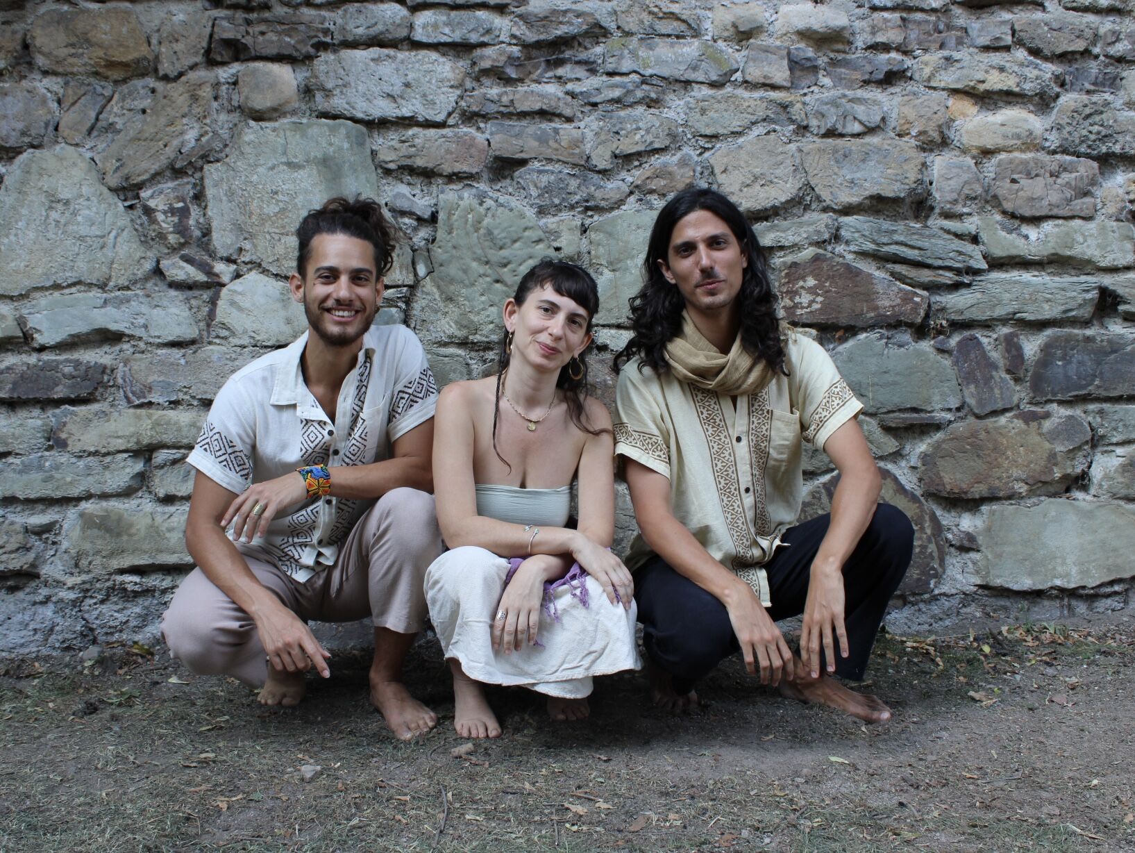 Yuli, Itay and Ben crouching barefoot in front of an old stone wall